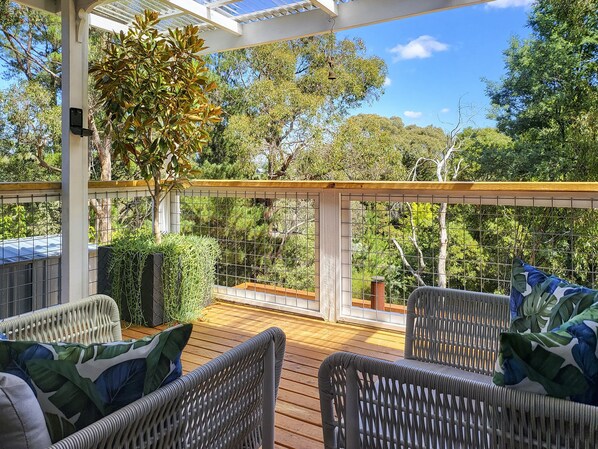 Une terrasse extérieure couverte, aménagée avec des meubles en osier et offrant une vue sur les arbres environnants.
