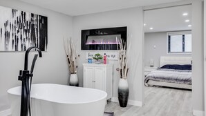 Un baño moderno con una bañera independiente, un tocador con espejo y un cuadro abstracto grande en la pared.