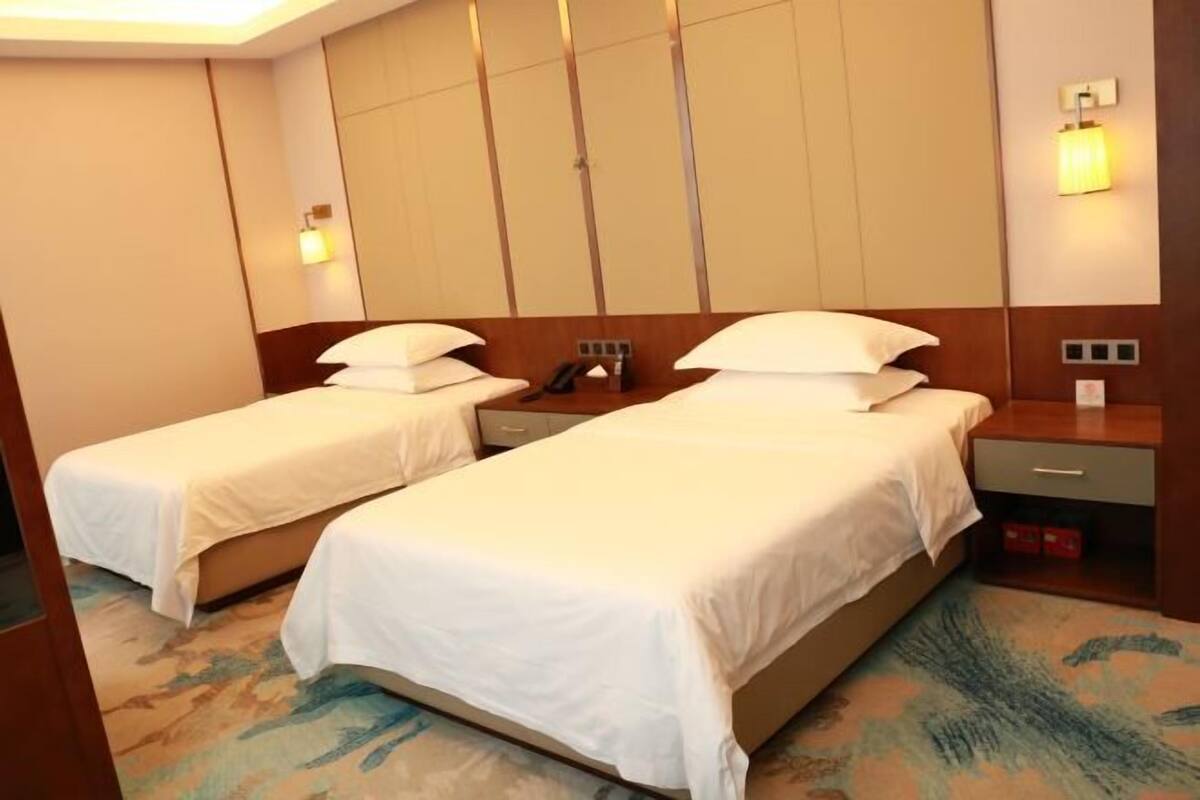 Une chambre d’hôtel avec deux lits simples, une table de chevet avec une lampe, un téléphone et un petit tiroir.
