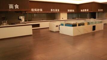 A modern hotel lobby with a reception desk, a seating area, and a counter with food options.
