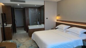 A hotel room with a large bed, a bedside table, a bathroom with a shower, and a small seating area. - Jincheng Hotel (Linqu)