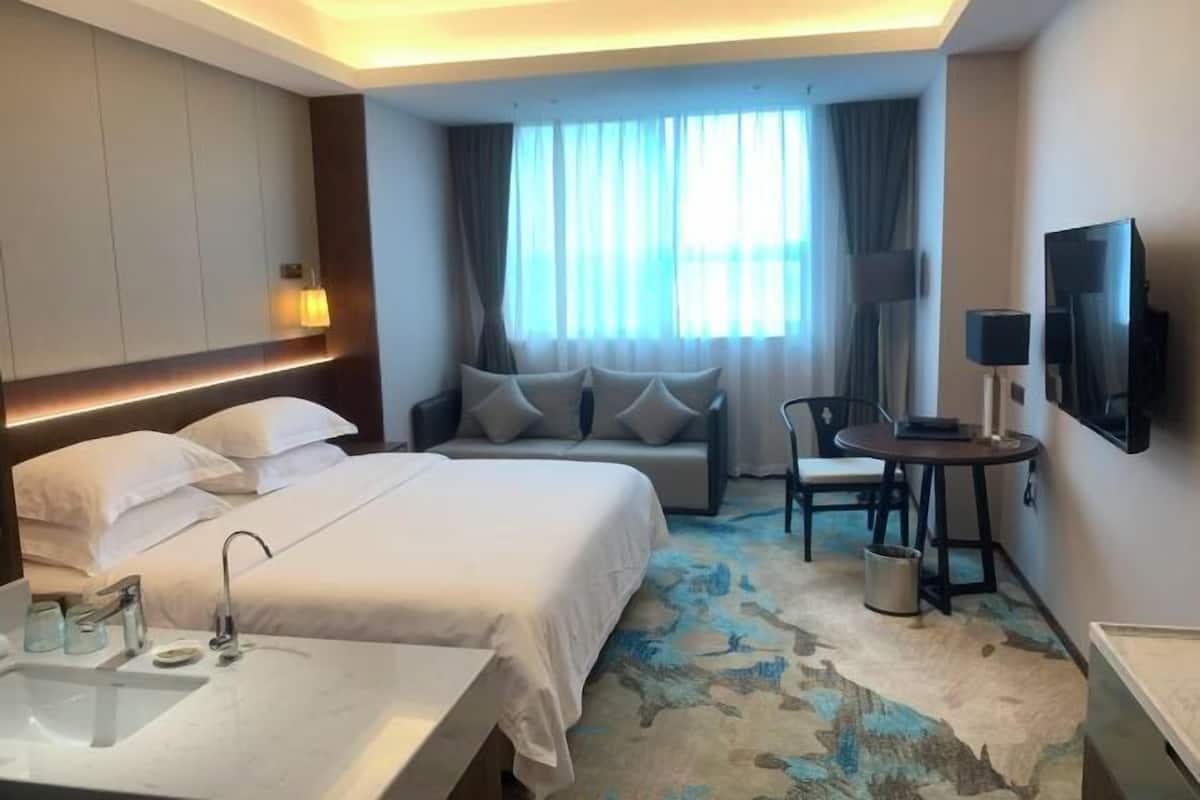 Une chambre d’hôtel avec un lit, un bureau, une chaise, une télévision et une grande fenêtre avec des rideaux.
