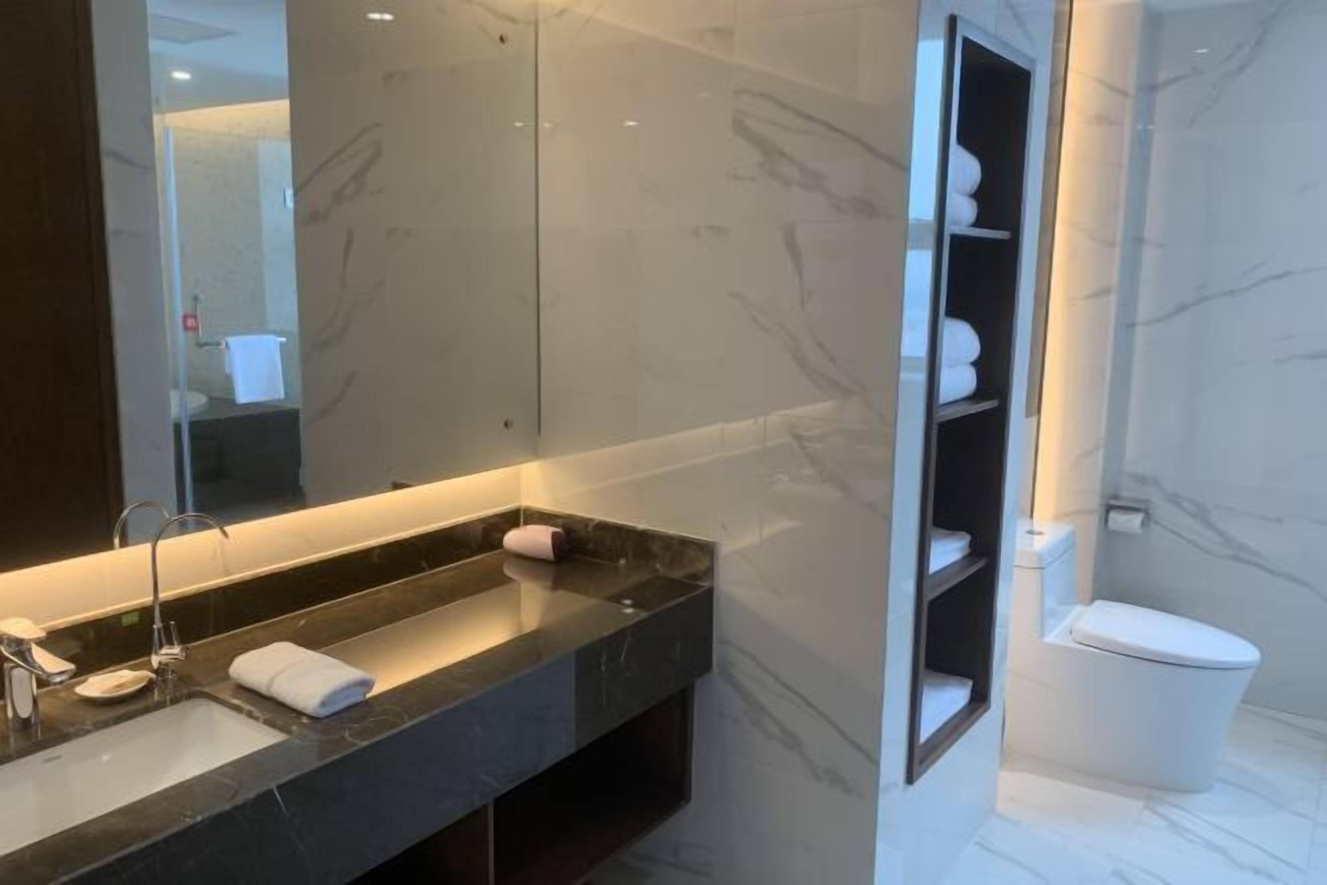 A modern bathroom with a marble sink, a large mirror, and a toilet.