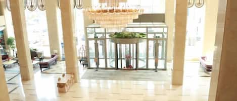 A spacious lobby with a large chandelier, a reception desk, and a view of the outside.