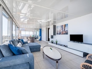 A modern living area with a sofa set, a coffee table, a TV, and a dining area with chairs and a table.