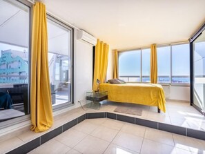 A modern bedroom with a large bed, a glass desk, and a view of the city.