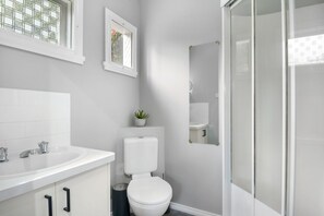 A modern bathroom with a white sink, toilet, and shower area. - Aurora Cottage at Hepburn Mineral Springs Reserve (Hepburn Springs)