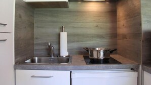Une cuisine compacte avec des meubles blancs, un évier en acier inoxydable, une cuisinière encastrée et un lave-vaisselle blanc.