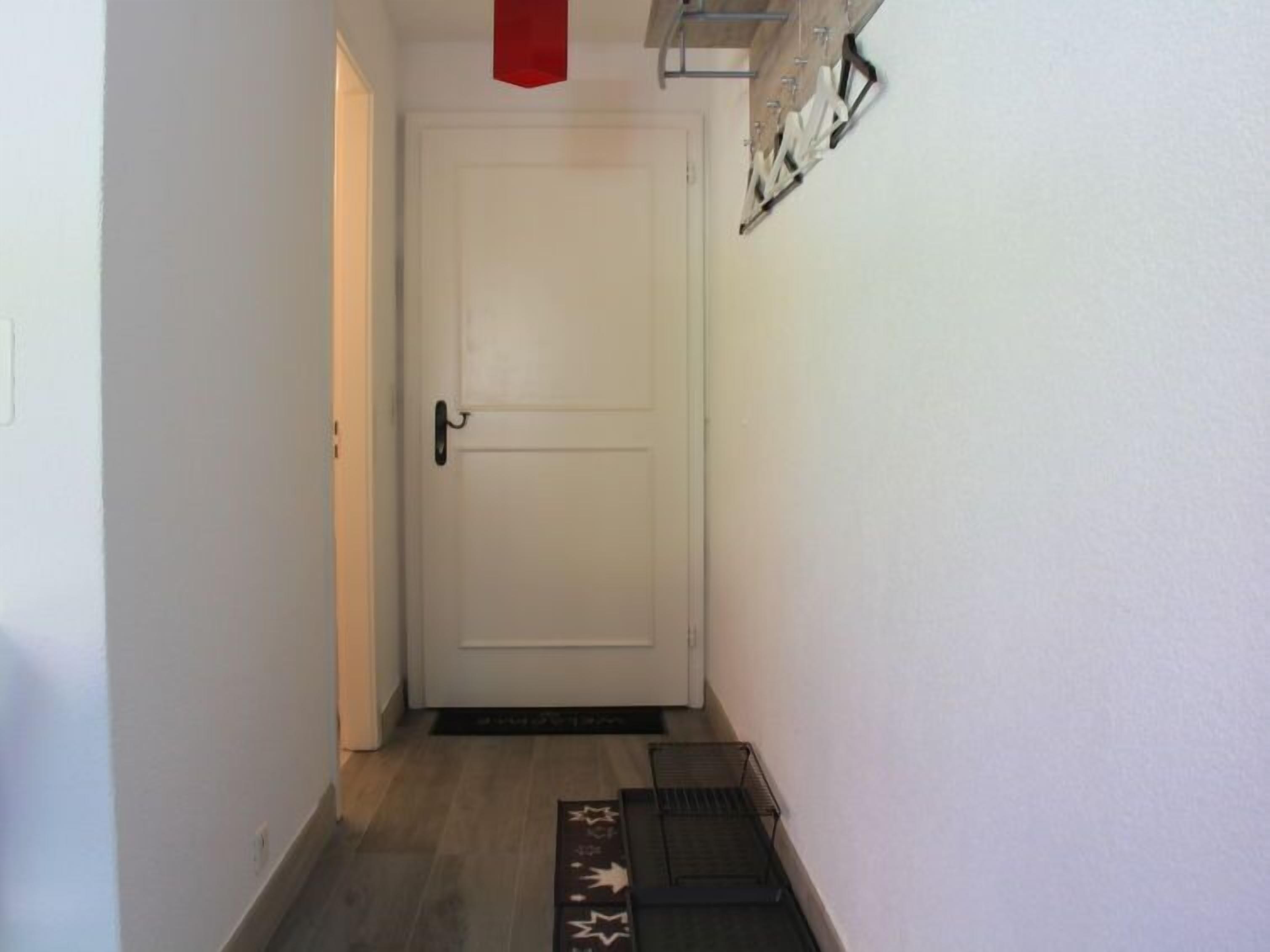 A narrow hallway with a white door, a black doormat, and a metal rack on the wall.