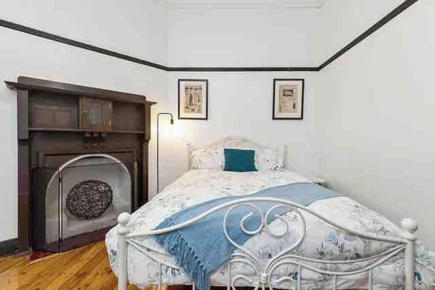 A bedroom with a bed, a fireplace, and two framed pictures on the wall.