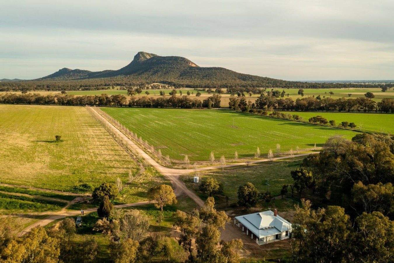 Uma propriedade rural com um extenso campo aberto, uma casa com telhado branco e uma montanha ao fundo.