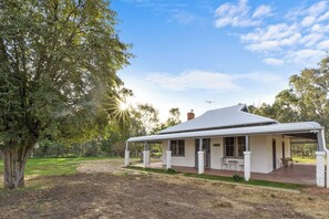 A single-story house with a covered porch, a chimney, and a small garden area. - The Homestead at Avalon Farmstay. Quiet cottage on working farm (The Rock)