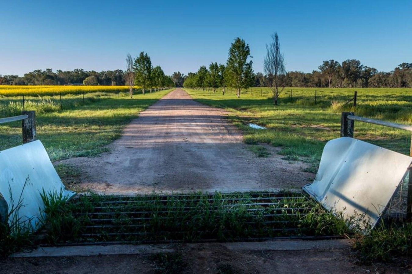 A rural pathway leading to a gate with a metal barrier and a fence on either side.