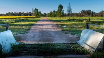 A rural pathway leading to a gate with a metal barrier and a fence on either side.