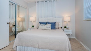 Een slaapkamer met een bed, twee nachtkastjes, een plafondventilator en een schuifdeur met glas.