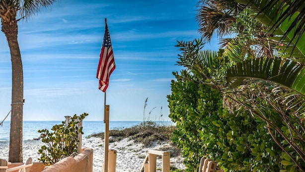 Uitzicht op het strand met een Amerikaanse vlag, palmbomen en zand.