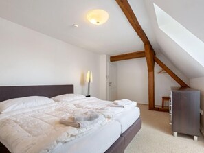Une chambre avec un grand lit, une lampe de chevet, une armoire et un plafond en pente avec des poutres en bois.