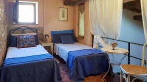 Une chambre avec deux lits, une petite table avec une chaise, une fenêtre avec des rideaux et un tableau au mur.