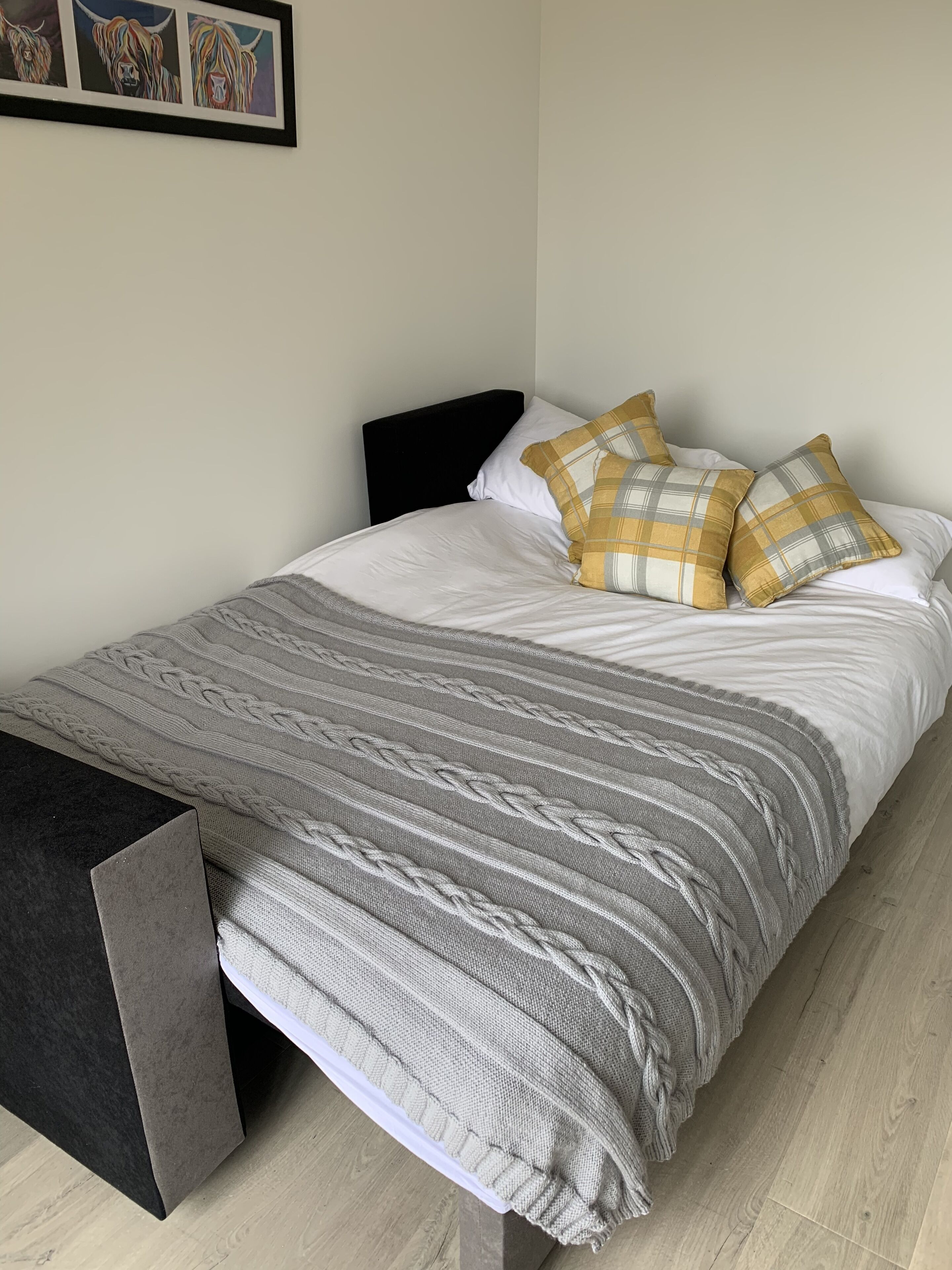 A neatly made bed with a grey and white striped blanket, two plaid pillows, and a black headboard.