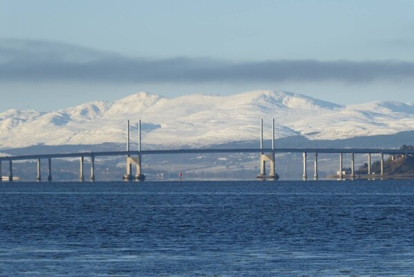 A bridge with multiple supports over a body of water, with snow-covered mountains in the background.