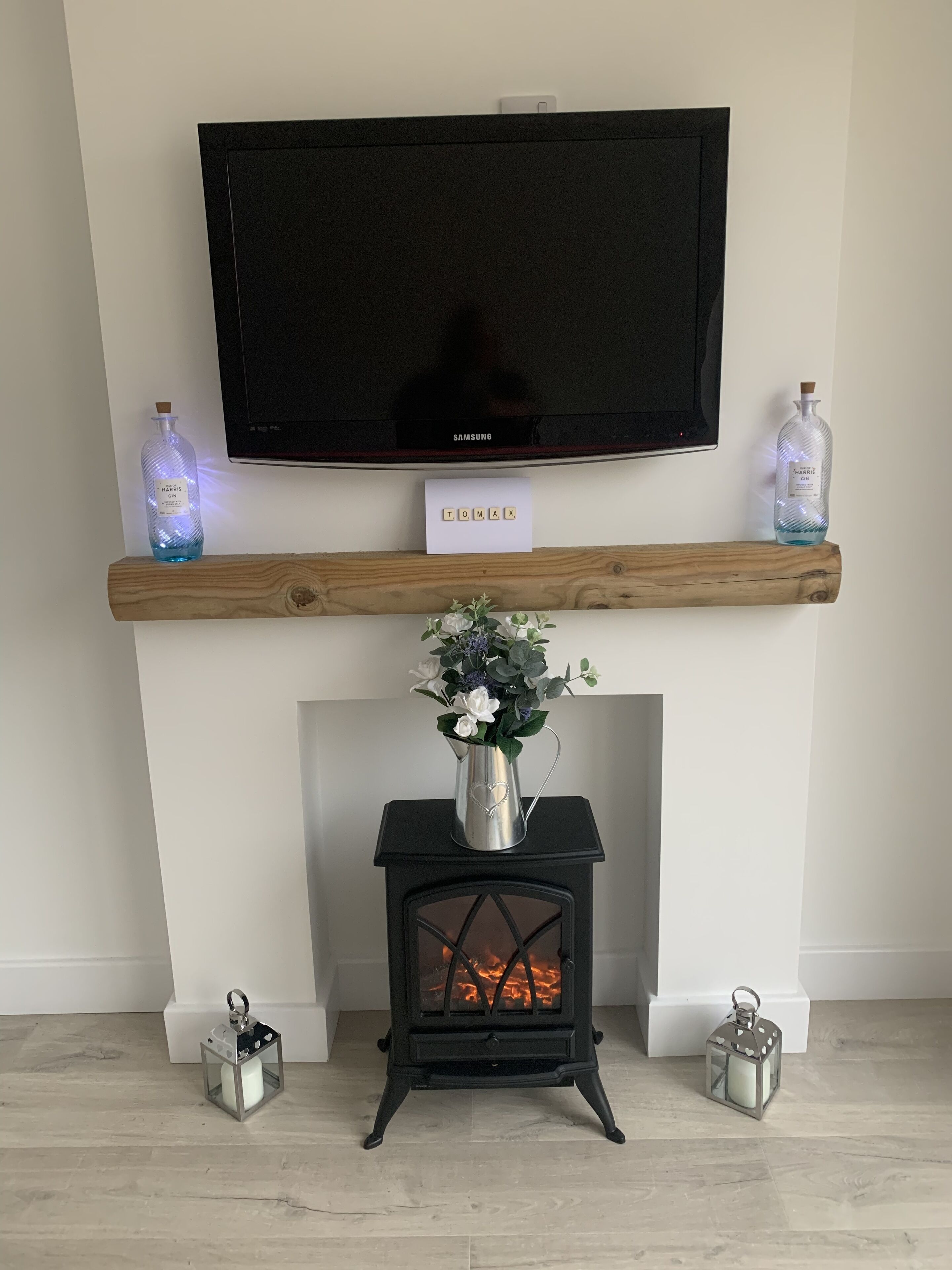 A fireplace with a TV mounted above it, a wooden mantel, and a vase with flowers.