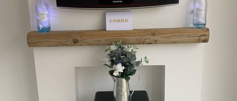 A fireplace with a TV mounted above it, a wooden mantel, and a vase with flowers.