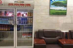 Una máquina expendedora con bebidas y aperitivos, un sofá de cuero marrón y un cuadro de un árbol en la pared.