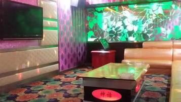A room with a flat-screen TV mounted on the wall, a sofa, a small table with a red circular object on it, and a patterned carpet.
