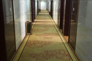 A corridor with patterned carpet, mirrored doors, and a trash bin.