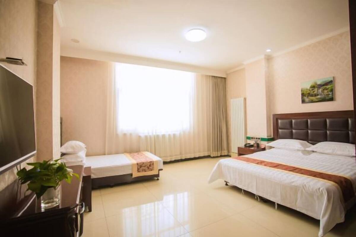 Habitación de hotel con una cama grande, otra más pequeña, un televisor, un escritorio y una ventana con cortinas.