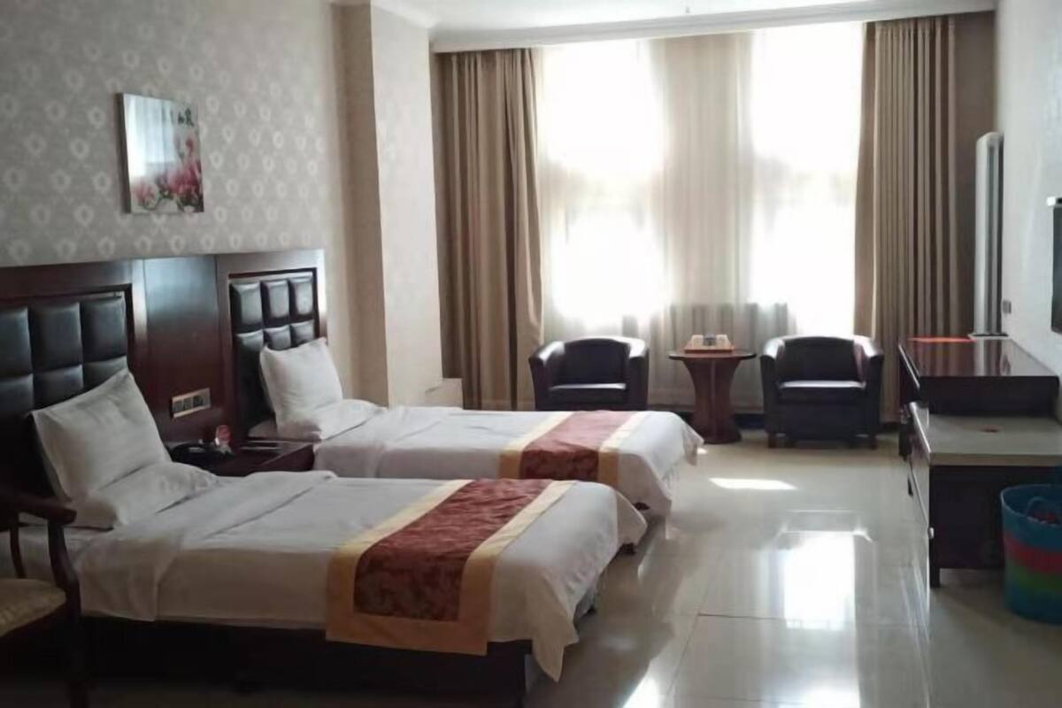 Habitación de hotel con dos camas, un escritorio, una silla, un televisor y una ventana con cortinas.