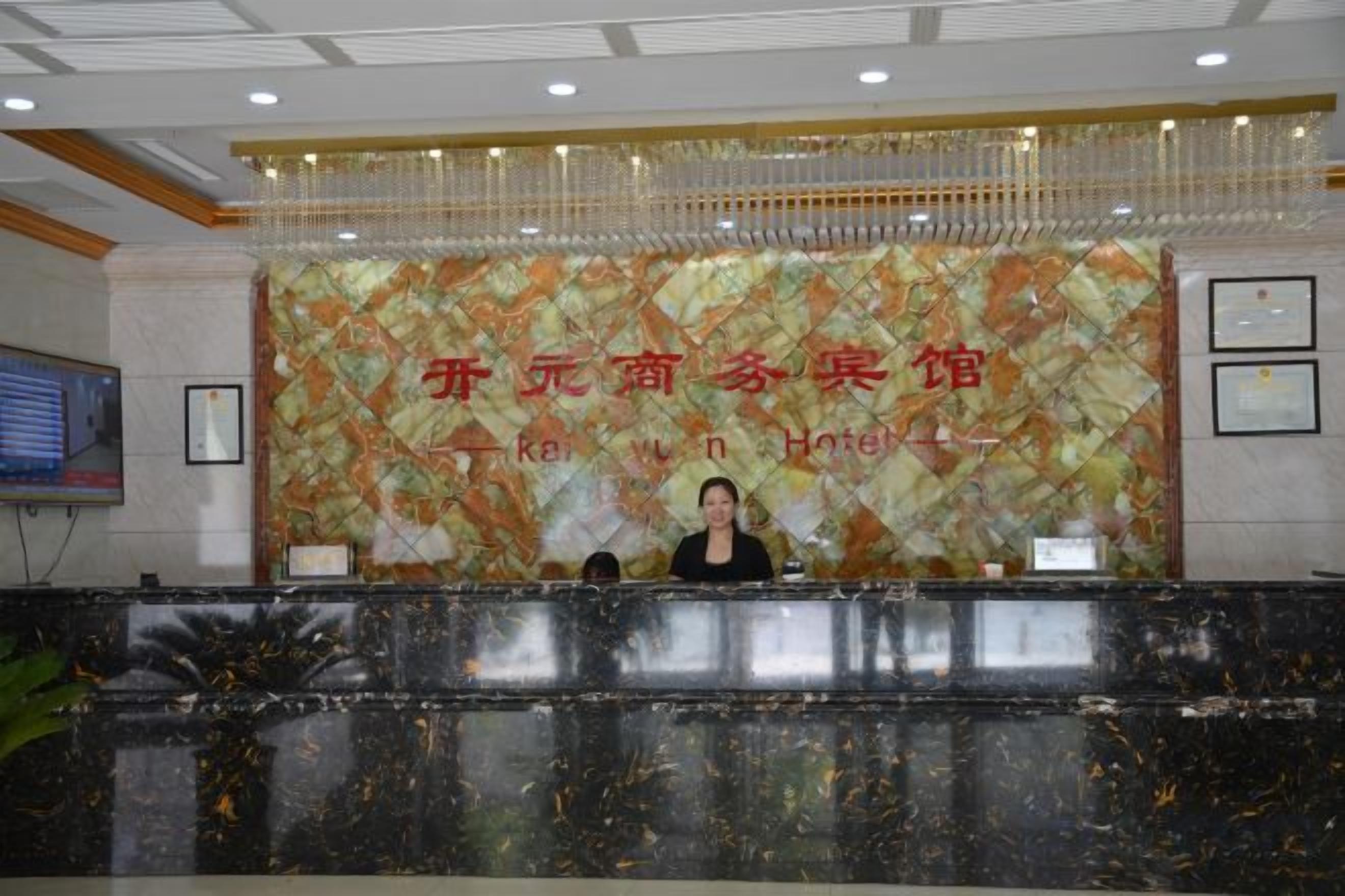 A hotel reception desk with a large, patterned backdrop and a receptionist seated behind it.