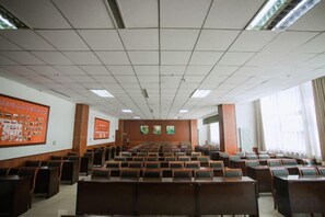 Un salón de conferencias con filas de sillas, una pantalla grande y un atril.