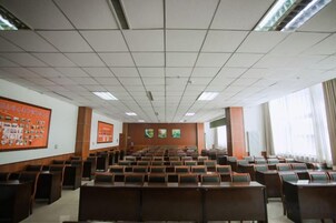 Un salón de conferencias con filas de sillas, una pantalla grande y un atril.