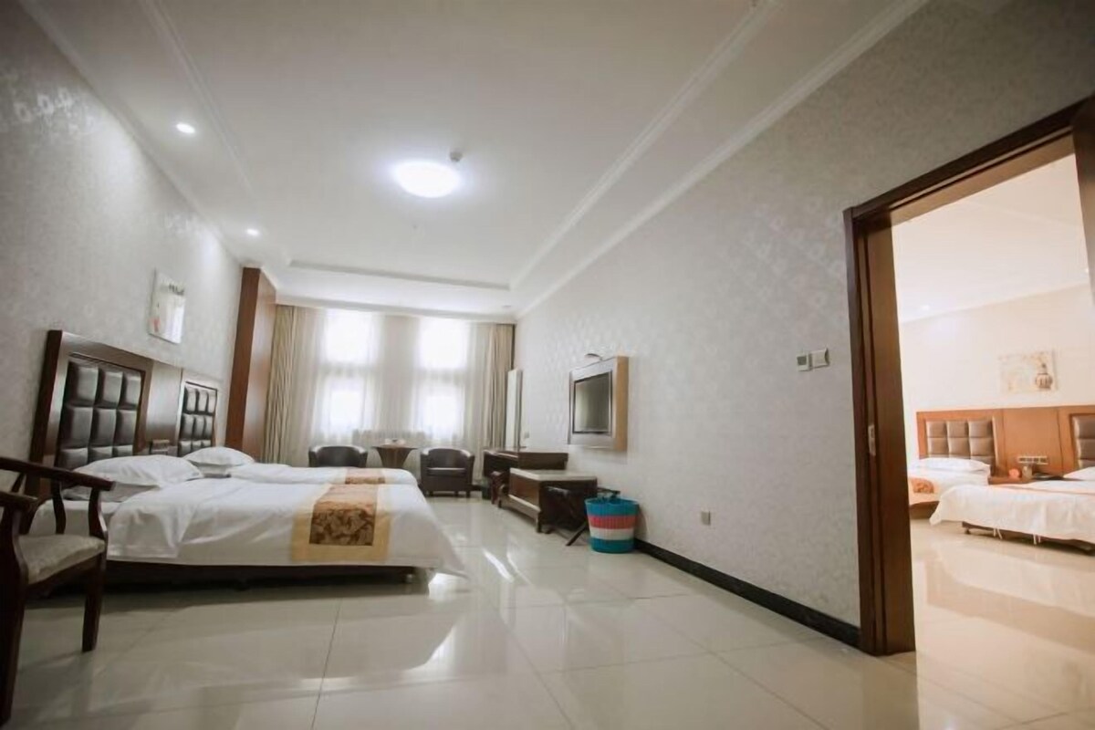Habitación de hotel con dos camas, un escritorio, una silla, un televisor y un ventanal grande.