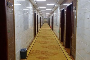 Un pasillo de hotel con alfombra estampada, paredes de mármol y puertas que dan a las habitaciones.