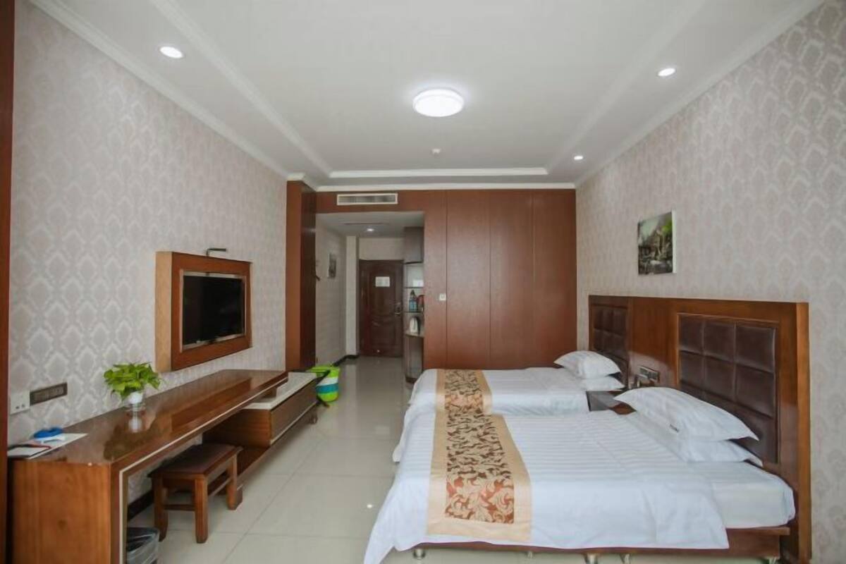 Habitación de hotel con dos camas, un escritorio, un televisor y un baño visible a través de una puerta abierta.