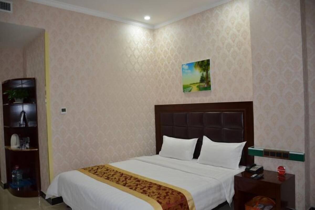 Una habitación de hotel con una cama, una mesita de noche, un estante con objetos y un cuadro en la pared.