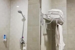 Une salle de bain avec une douche, un porte-serviettes avec des serviettes pliées et un distributeur de savon.