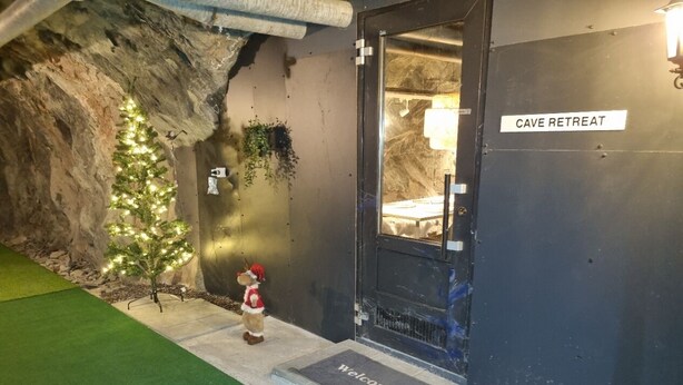 A cave-themed entrance with a 'Cave Retreat' sign, a welcome mat, and a Christmas tree with lights.