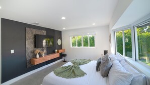 A modern bedroom with a large bed, a mounted TV, and a window with a view of greenery. - MAGR LUXURY (Cutler Bay)