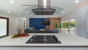 A modern kitchen with a central island, a built-in stove, and a glass-enclosed range hood. - MAGR LUXURY (Cutler Bay)