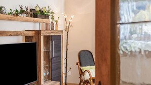 A living room with a flat-screen TV, wooden shelves with decorative items, a chair, and a plant. - Holiday Apartment Waldruhe with Balcony, Mountain View & Wi-Fi (Garmisch-Partenkirchen)