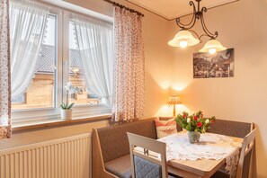 A dining area with a table, chairs, a vase with flowers, a lamp, and a window with curtains.