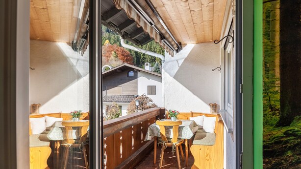 A wooden deck with a table and chairs, a wooden bench, and a view of a house and trees. - Holiday Apartment Waldruhe with Balcony, Mountain View & Wi-Fi (Garmisch-Partenkirchen)