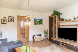 A living room with a sofa, a wooden cabinet, a TV, and a painting of a mountain landscape.