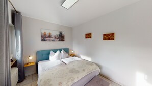 Une chambre à coucher comprenant un lit, deux tables de chevet, une commode, une fenêtre avec des rideaux et deux œuvres d’art accrochées au mur.