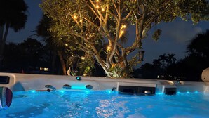 Ein Bereich mit Whirlpool, einem Baum und Lichterketten, umgeben von Palmen.