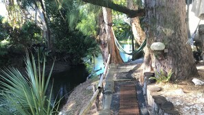 Ein Holzweg führt zu einer Hängematte, umgeben von Bäumen und einem kleinen Wasserspiel.