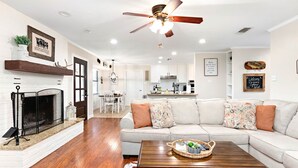 Un salon moderne avec une cheminée, un ventilateur de plafond et un coin repas à l’arrière-plan.